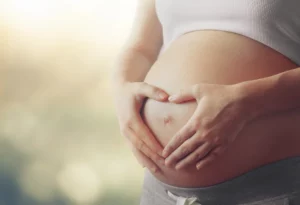 Pregnant woman holding her hands in the shape of a heart over pregnant belly acupuncture for anxiety during pregnancy