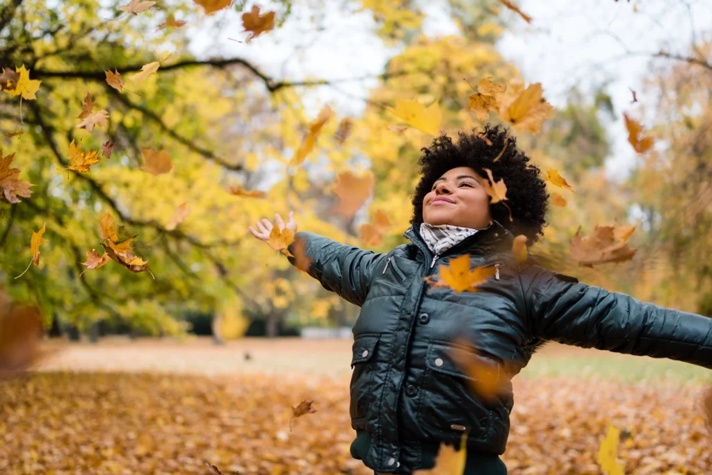 Smiling woman in park, arms outstretched.